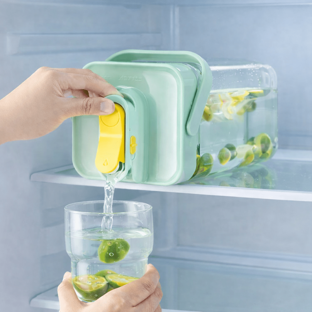 Person pouring water from a green container into a glass with lime slices inside a refrigerator.