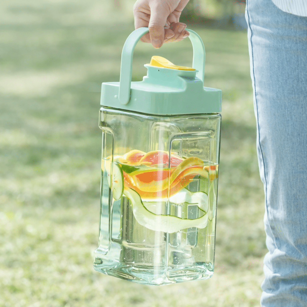 Clear water bottle with fruit infusers held by a person outdoors
